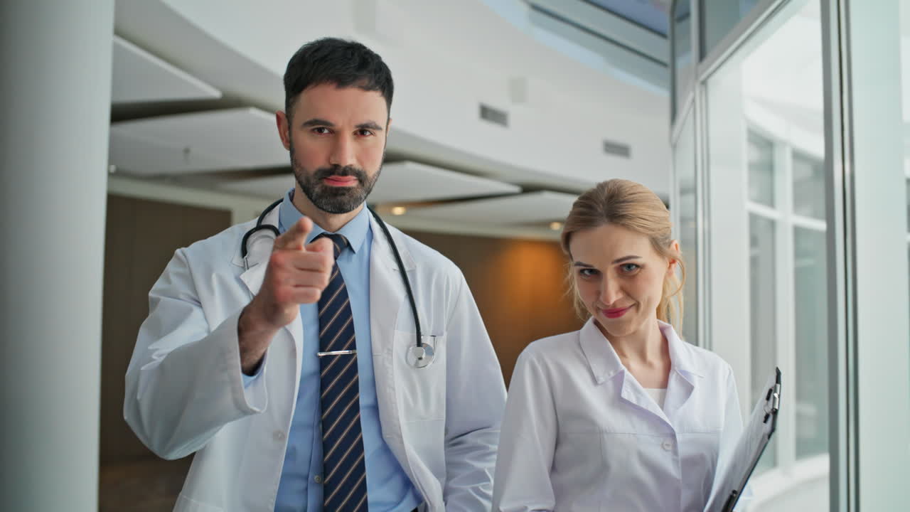 Dois médicos andando pelo corredor da clínica em close-up. Homem barbudo com estetoscópio apontando.