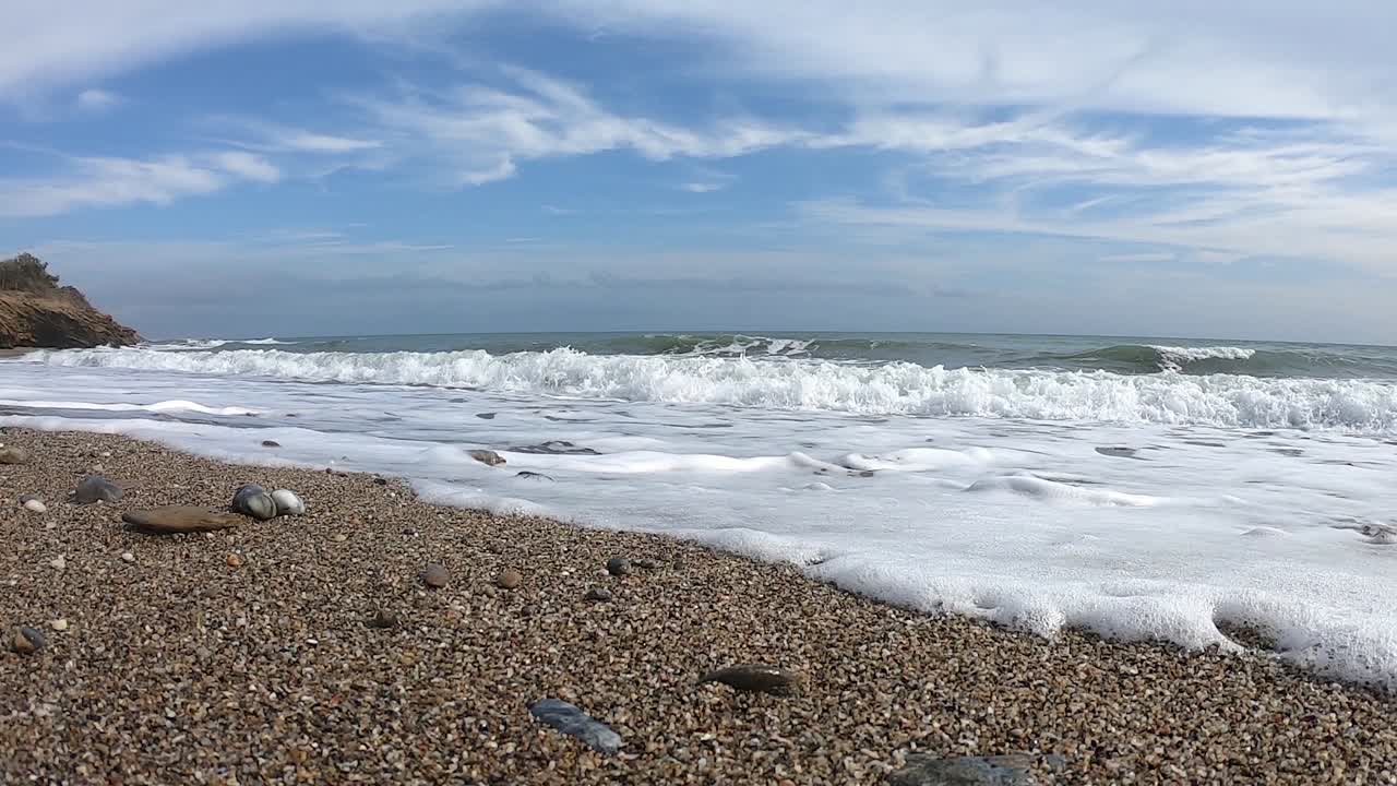 파도와 거품이 있는 모래 해변과 바위, 흰 구름이 있는 푸른 하늘, 슬로우 모션 영상