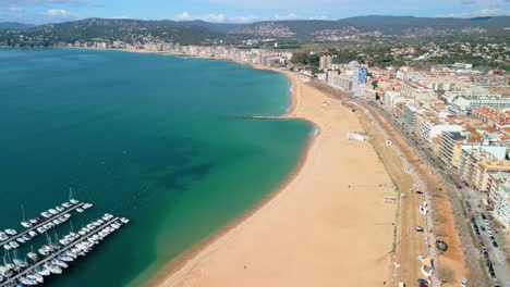 High-above,-Palamós-reveals-its-dynamic-waterfront-promenade-lined-with-palm-trees,-inviting-leisurely-strolls-along-the-coast