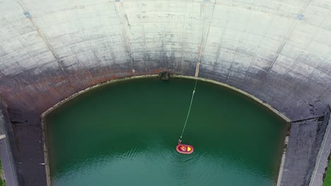 Aerial-drone-view-of-a-person-hanging-on-a-bungee-jumping-cord-rope-to-50m-high-dam-platform-while-a-raft-come-closer-to-get-him-aboard