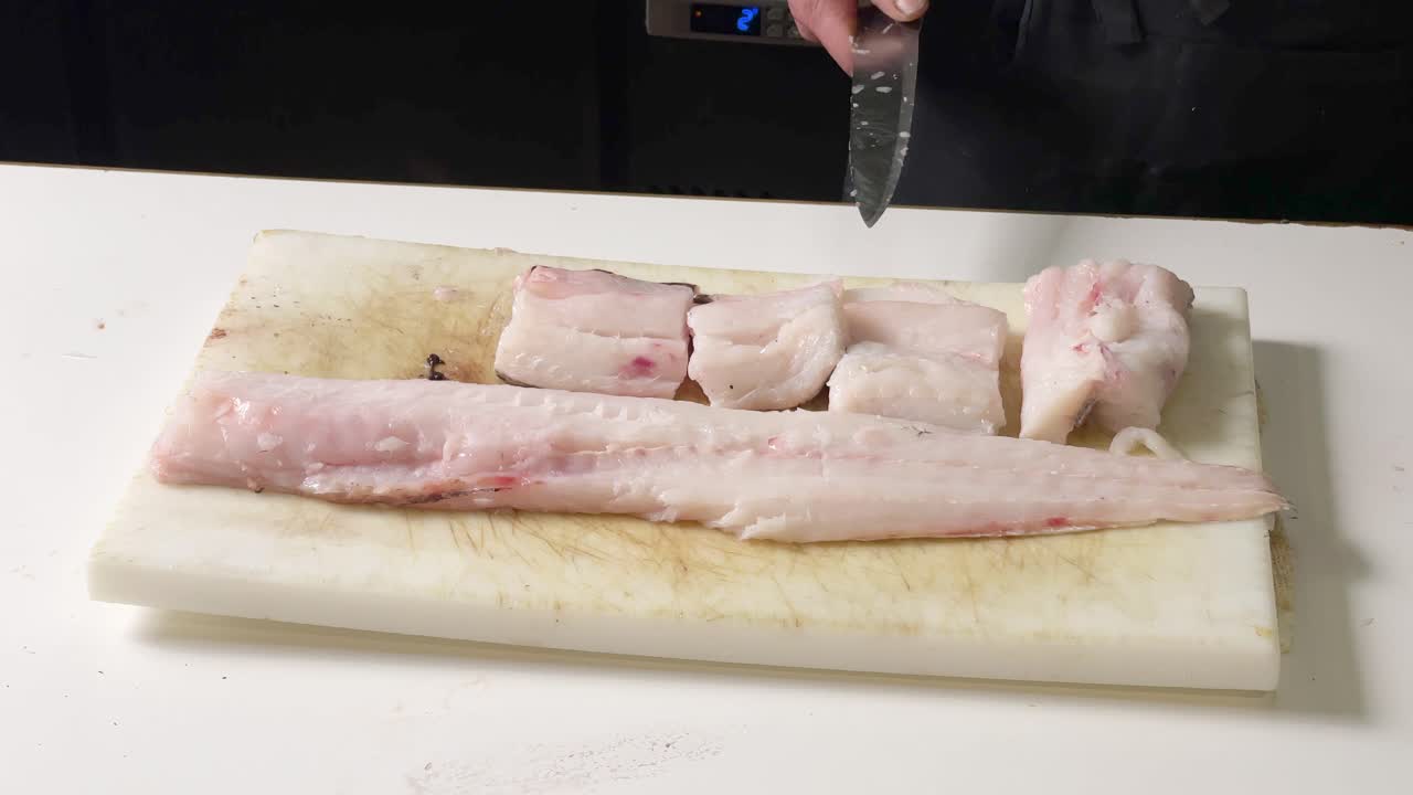 저녁 식사를 위해 굽기 전에 스페인 레스토랑에서 생 대구를 자르는 전문 남자 요리사의 손을 닫습니다