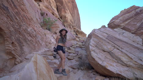 young female with photo camera walking down the rocky hill in valley of fire state park, nevada usa, slow motion