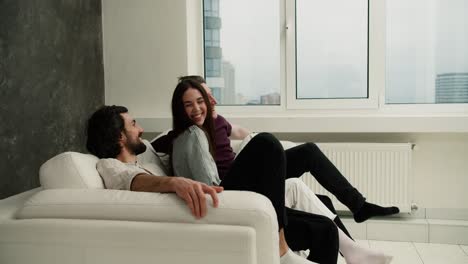 friendship, new home concept - smiling male and female friends are falling on the new white sofa together