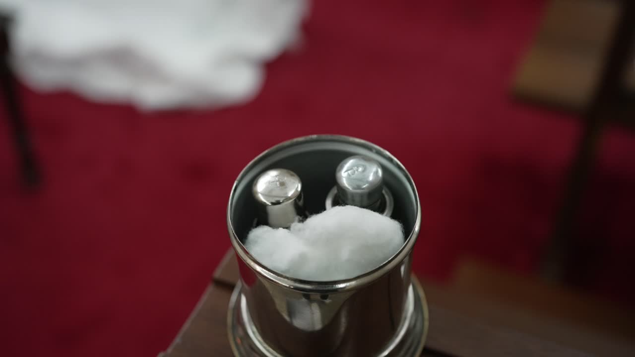 Close-up de recipiente de prata para óleo sagrado com algodão para ritual de batismo sobre tapete vermelho