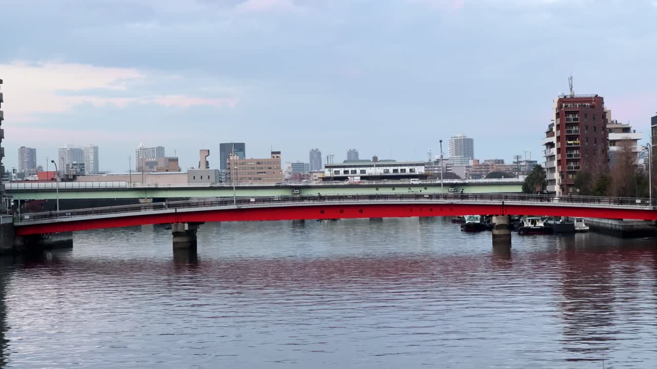 A red bridge over a calm river in Harumi, Tokyo, with a cityscape in the background