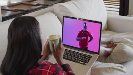 Mujer-Birracial-Mirando-Una-Computadora-Portátil-Con-Un-Jugador-De-Rugby-Afroamericano-Atrapando-Una-Pelota-En-La-Pantalla