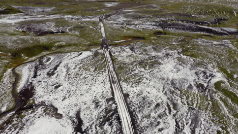 aerial follow of white car driving on a mountain road partially covered with snow