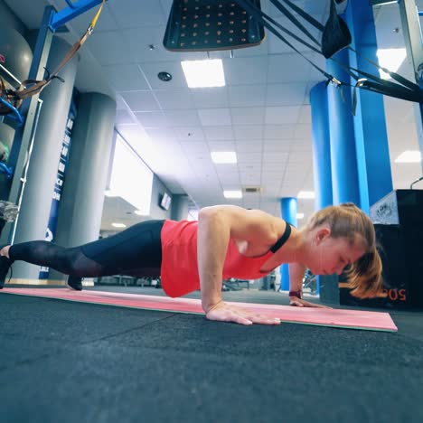 athletic woman does push-ups as part of workout. girl in sportswear doing push-up exercise on a mat in the fitness centre.