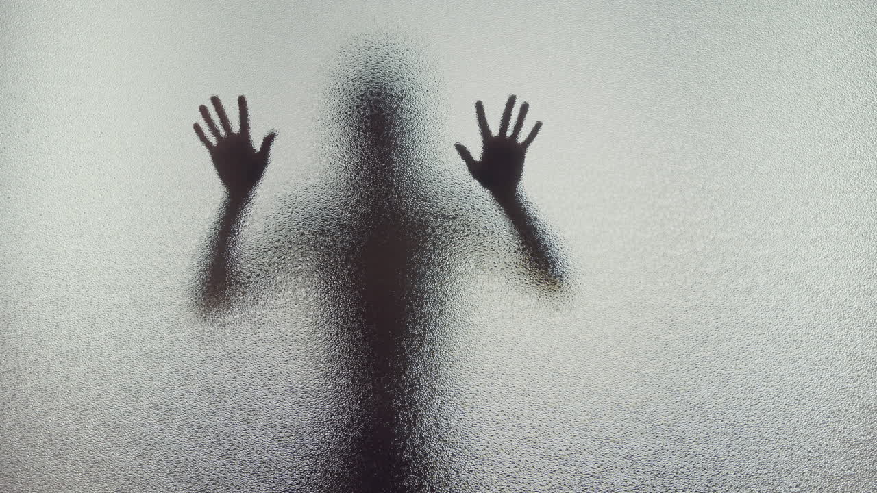 A female silhouette behind the frosted window touches the glass slowly