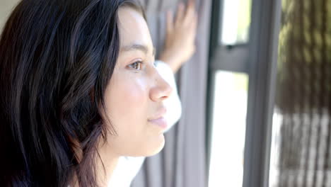 happy biracial teenage girl drawing curtains, looking out of sunny window, copy space, slow motion