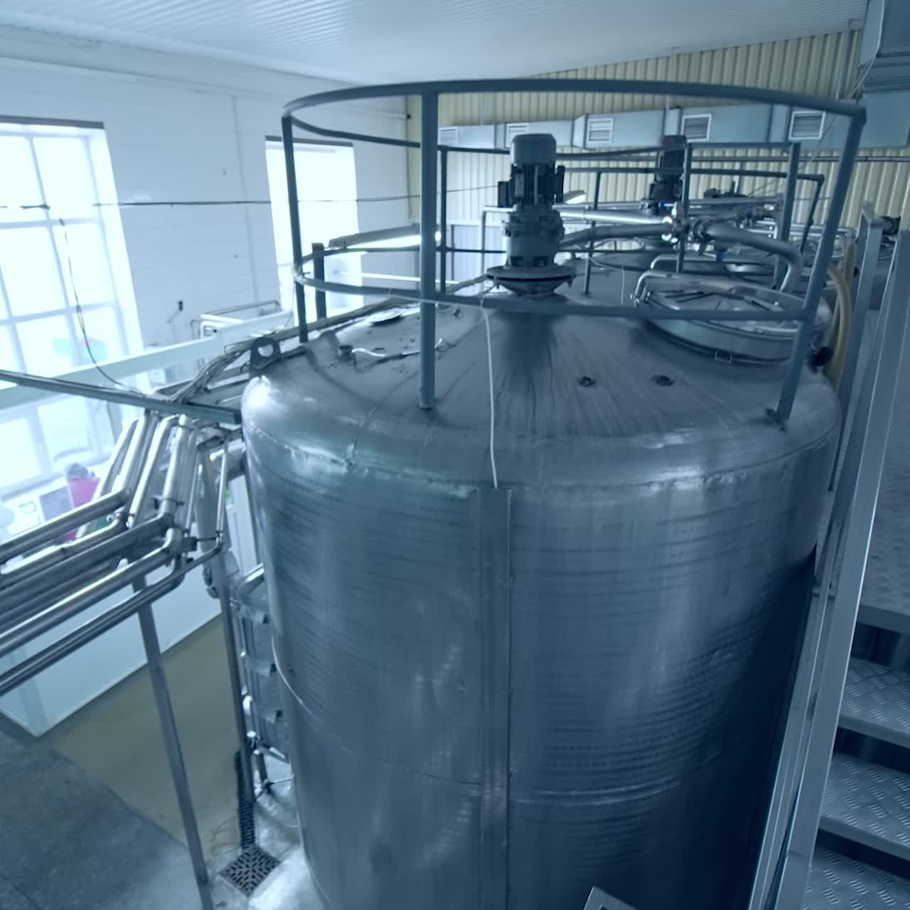 Numerous steel pipes leading to a huge reservoir at the milk factory. Modern milk factory interior for processing milk. View from the above