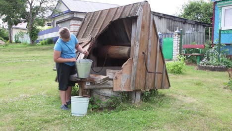 the boy takes a bucket of water from the well and pours it into another.