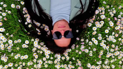 Una-Hermosa-Mujer-Acostada-En-Una-Cama,-Margaritas-Con-Flores-En-Su-Largo-Cabello-Negro,-Mirando-Hacia-Arriba-Con-Gafas-De-Sol