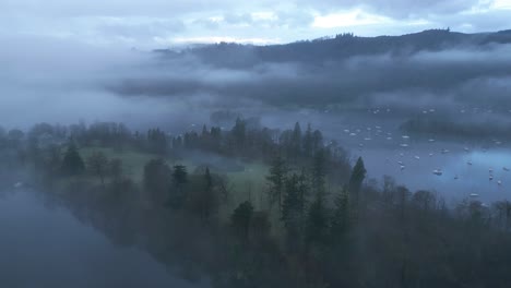 drone strafing over the lakeside of windermere lake, showing a misty and foggy village located in the county of cumbria, in great britain