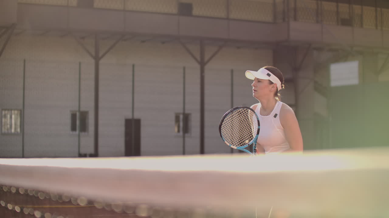 테니스 공을 기다리는 즐거운 운동선수: 숙련된 여성 테니스 선수가 공을 때리기 위해 준비하고 있습니다. 그녀는 라켓을 들고 포즈를 취하고 있습니다. 여성은 테니스에 서 있습니다.