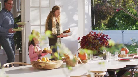 video of happy caucasian parents, daughter and grandfather bringing food to table for family meal