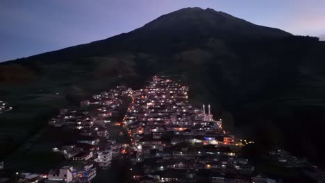 Aerial-night-shot-of-village-on-the-slope-of-mountain-with-light-on-with-slightly-foggy-weather