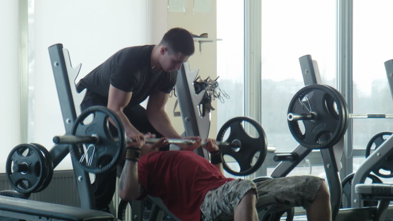 Man performing bench press with a trainer