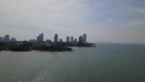 imágenes aéreas inversas del santuario de la verdad en una silueta y frente a la playa con condominios de gran altura en el fondo mientras un bote acelera a la derecha, pattaya, chonburi, tailandia