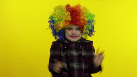 little child girl clown in colorful wig making silly face with eyes. fool around, smiling. halloween