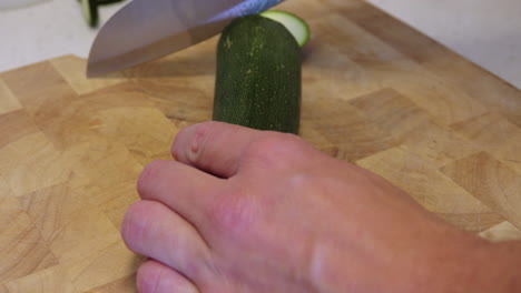 Zucchini-getting-cut-by-a-sharp-knife-on-a-wooden-board-on-a-white-marble-kitchen-counter-top