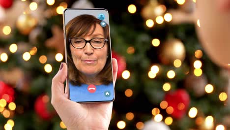 Frau-Mit-Smartphone-Führt-Zu-Weihnachten-Ein-Videogespräch.-Weihnachts-,-Technologie--Und-Feiertagskonzept-–-Nahaufnahme-Einer-Jungen-Frau-Mit-Smartphone,-Die-Zu-Hause-Ein-Videogespräch-Mit-Ihrer-älteren-Mutter-Führt