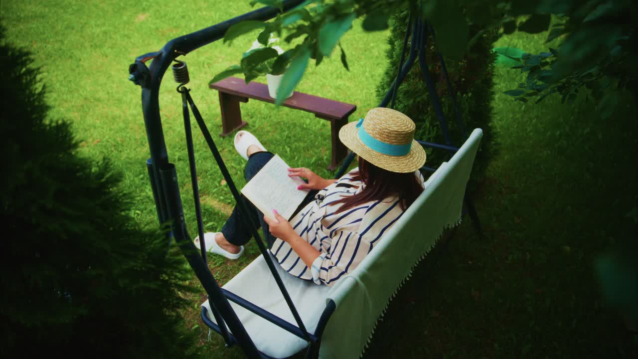 Woman relaxing on a swing chair in a garden, enjoying a book surrounded by greenery