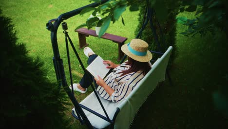 woman relaxing on a swing chair in a garden, enjoying a book surrounded by greenery