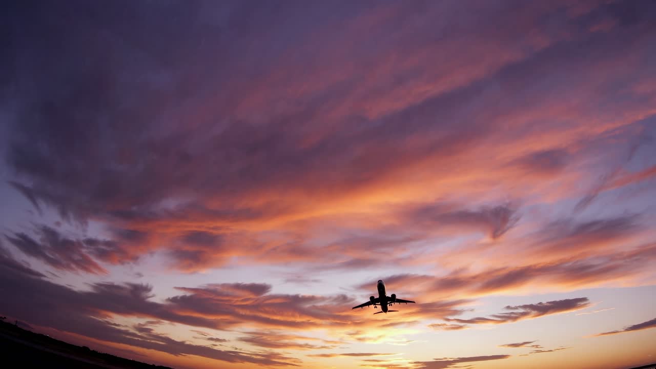 Wide-angle shot of a plane silhouetted against a vibrant sunset sky, capturing a cinematic