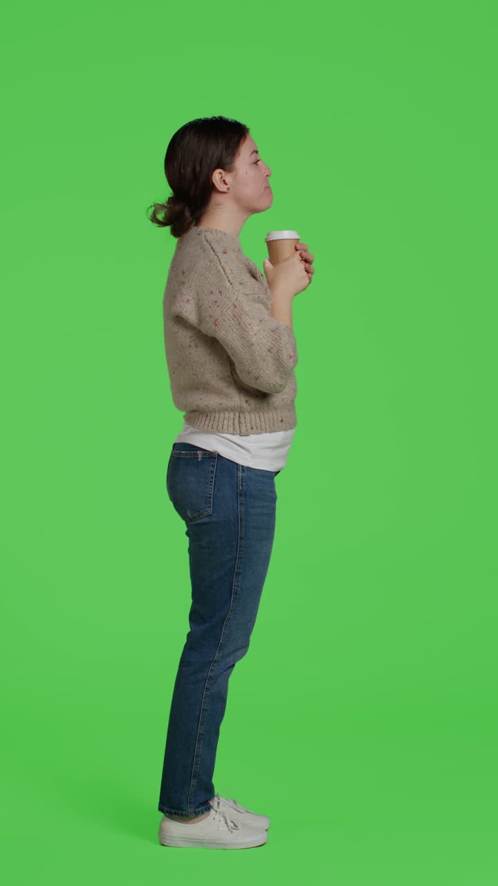 Vertical video: Profile of smiling adult drinking cup of coffee over full body green screen