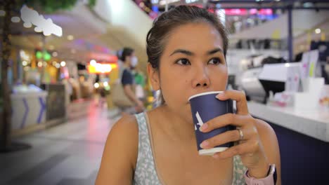 thai asian woman drinking coffee at a café in a shopping mall