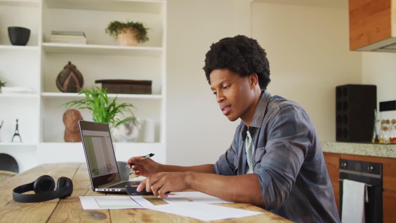 African american man working from home and using laptop and smartphone