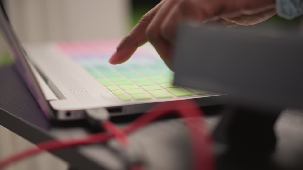 dj laptop pad controller finger tapping closeup outdoor setup colorful grid of pads with rgb lights red cable connection shallow depth of field hand pressing pads for beat triggering calm focused