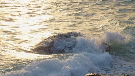 sunlit ocean waves breaking against the stone during sunset