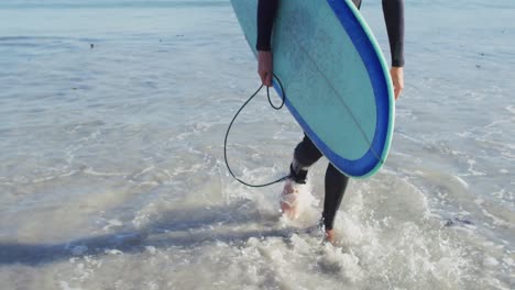 video of low section of caucasian man in wetsuit with surfboard walking out of sea on sunny beach