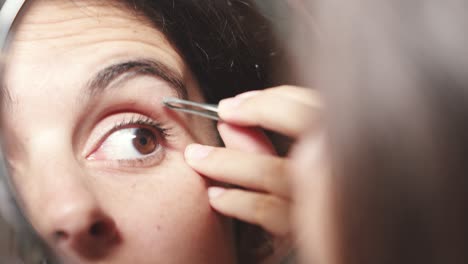 young woman plucks her hair from her eyebrows and looks in the mirror