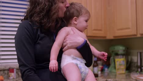 a mother undresses her little boy and he walks around the kitchen in his diaper