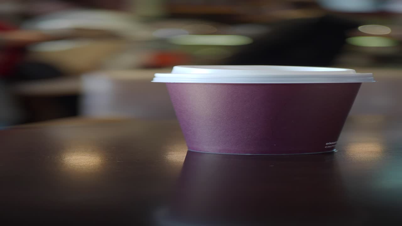 una taza de café de papel púrpura con una tapa blanca sentada en una mesa