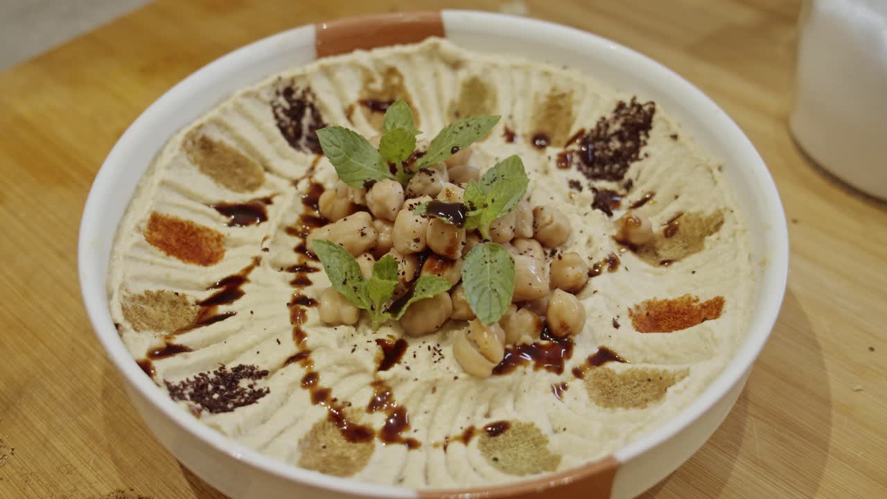 decorar plato de hummus con comino, pimentón, especias de romero a mano agregando pimentón, romero y menta fresca