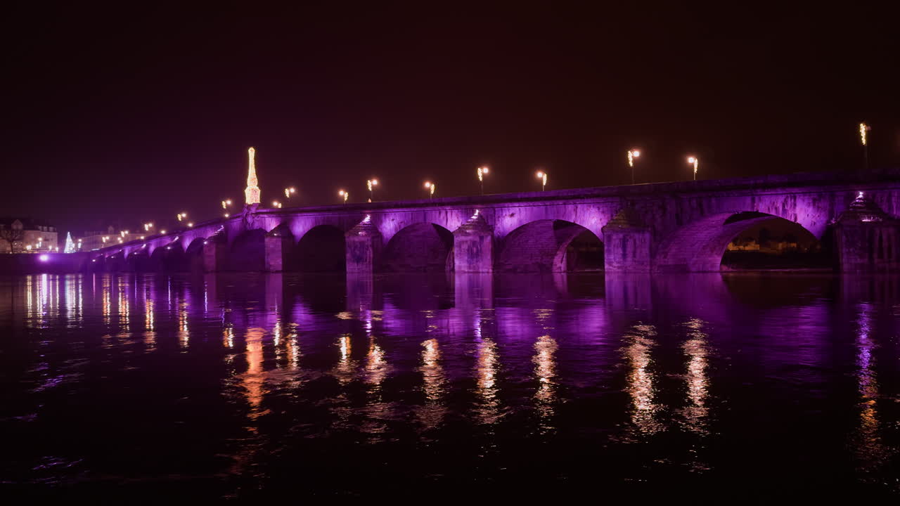 un hermoso puente de piedra arqueado iluminado en púrpura, reflejado en un río tranquilo por la noche