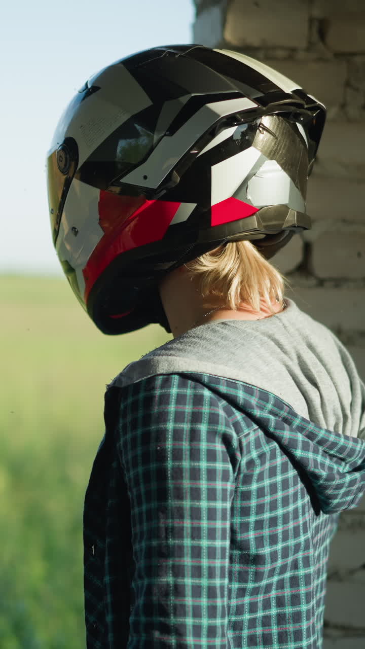 dos mujeres con cascos de pie cerca de la apertura de un edificio abandonado, mirando hacia un campo de hierba