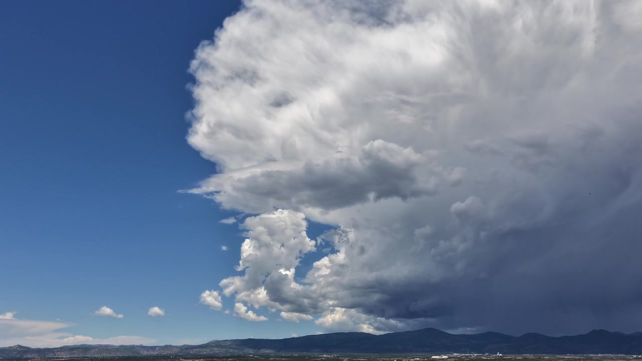 Un timelapse meteorológico dramático que captura una enorme tormenta monzónica moviéndose a través de una cordillera del Suroeste. Nubes densas cubren los picos, mostrando patrones climáticos dinámicos.