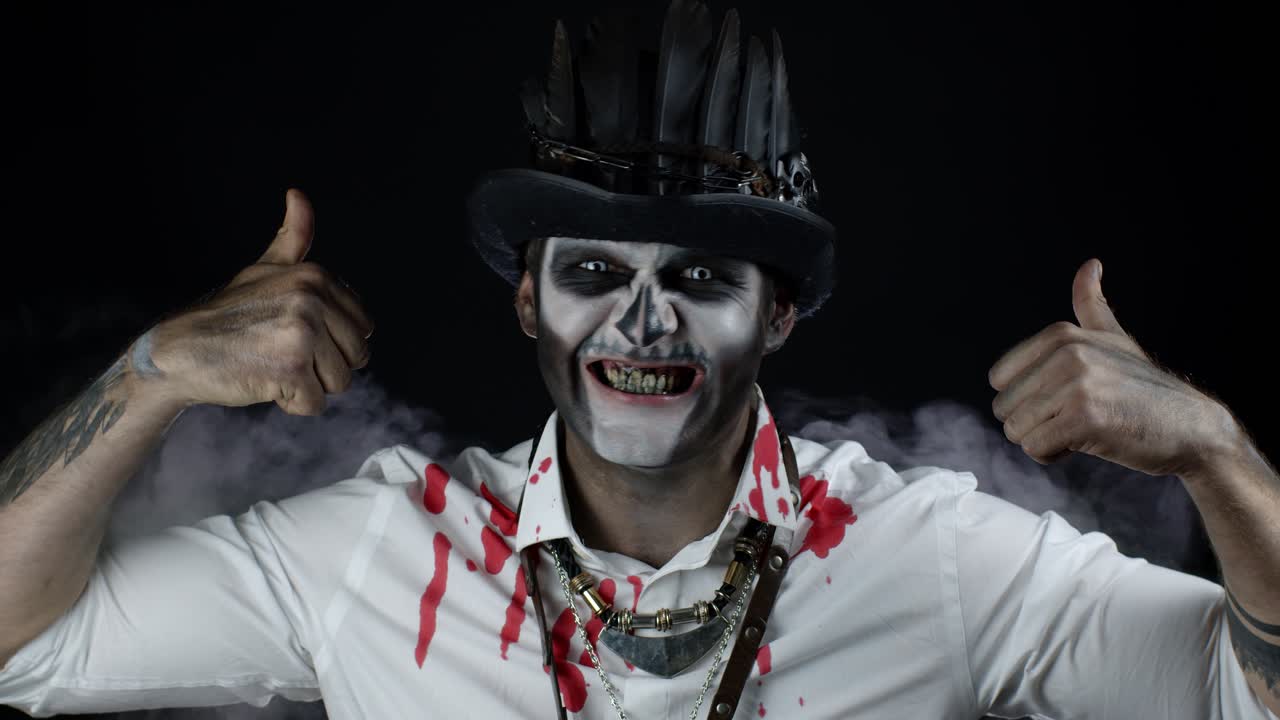 스레트 할로윈 의상을 입은 무서운 미소 짓는 남자가 엄지손가락을 나타내는 몸짓. 검은 바탕