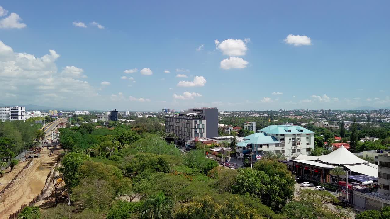 Aerial drone view of the cityscape of Santiago de los Caballeros. Features modern buildings, green parks, and construction zones under a blue sky in the Dominican Republic