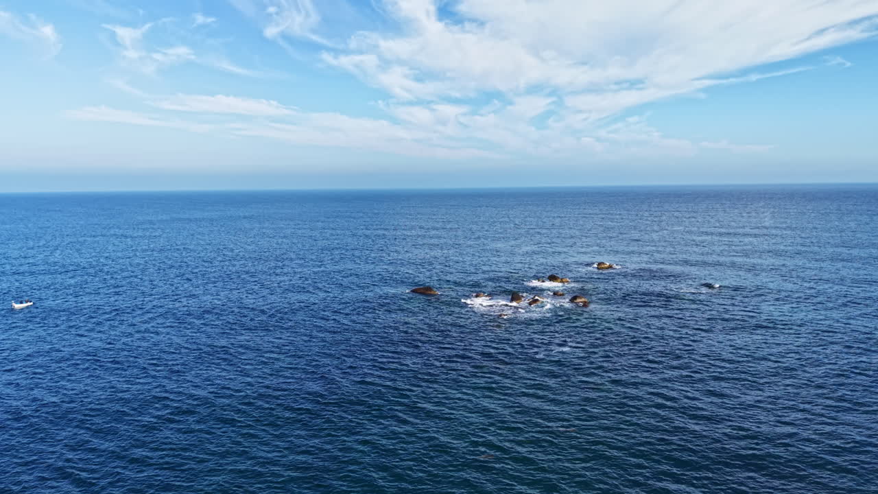 真昼、輝く太陽の下、青い海が空と溶け合い、穏やかな波立つ静かな水面には小さなボートが点在している。