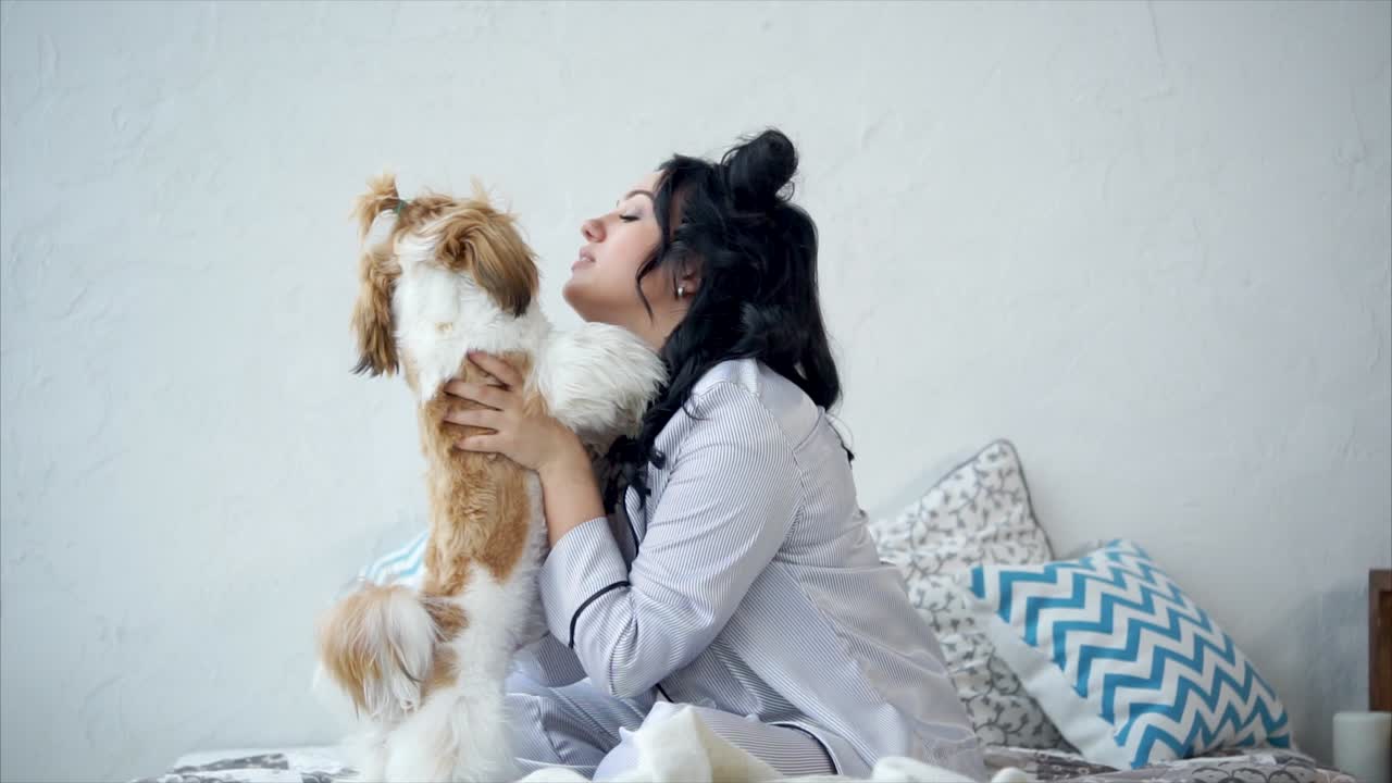 Woman cuddling with her Shih Tzu dog in pajamas on a bed