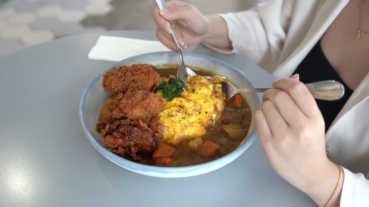 mujer joven cavando en un tazón de delicioso omurice japonés con salsa de curry y pollo frito con suero de leche crujiente, primer plano de movimiento de mano