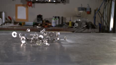 screws, washers and nuts falling in on a metal worker’s table in super slow motion