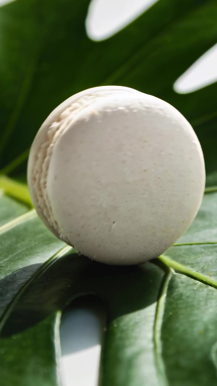 Vertical video: Rolling from small shift, white macaron moving left on studio leaf, showing filling