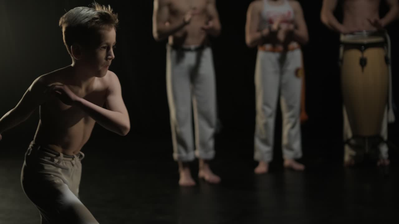 프로 댄서 그룹이 어 속에서 카포에이라를 연습하고 있으며, 스튜디오의 검은 바탕에 스포트라이트가 있습니다. 댄스의 요소를 결합하는 아프리카-브라질 무술입니다.